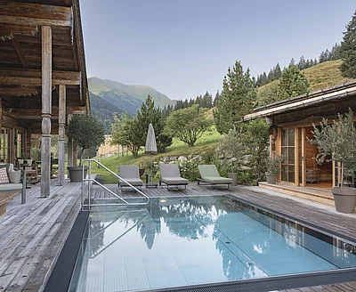Outdoor-Pool des Chalet Die Schmiedalm in Saalbach Hinterglemm im Sommer mit Chalet und Bergpanorama.