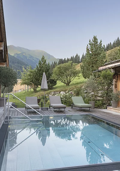 Outdoor-Pool des Chalet Die Schmiedalm in Saalbach Hinterglemm im Sommer mit Chalet und Bergpanorama.