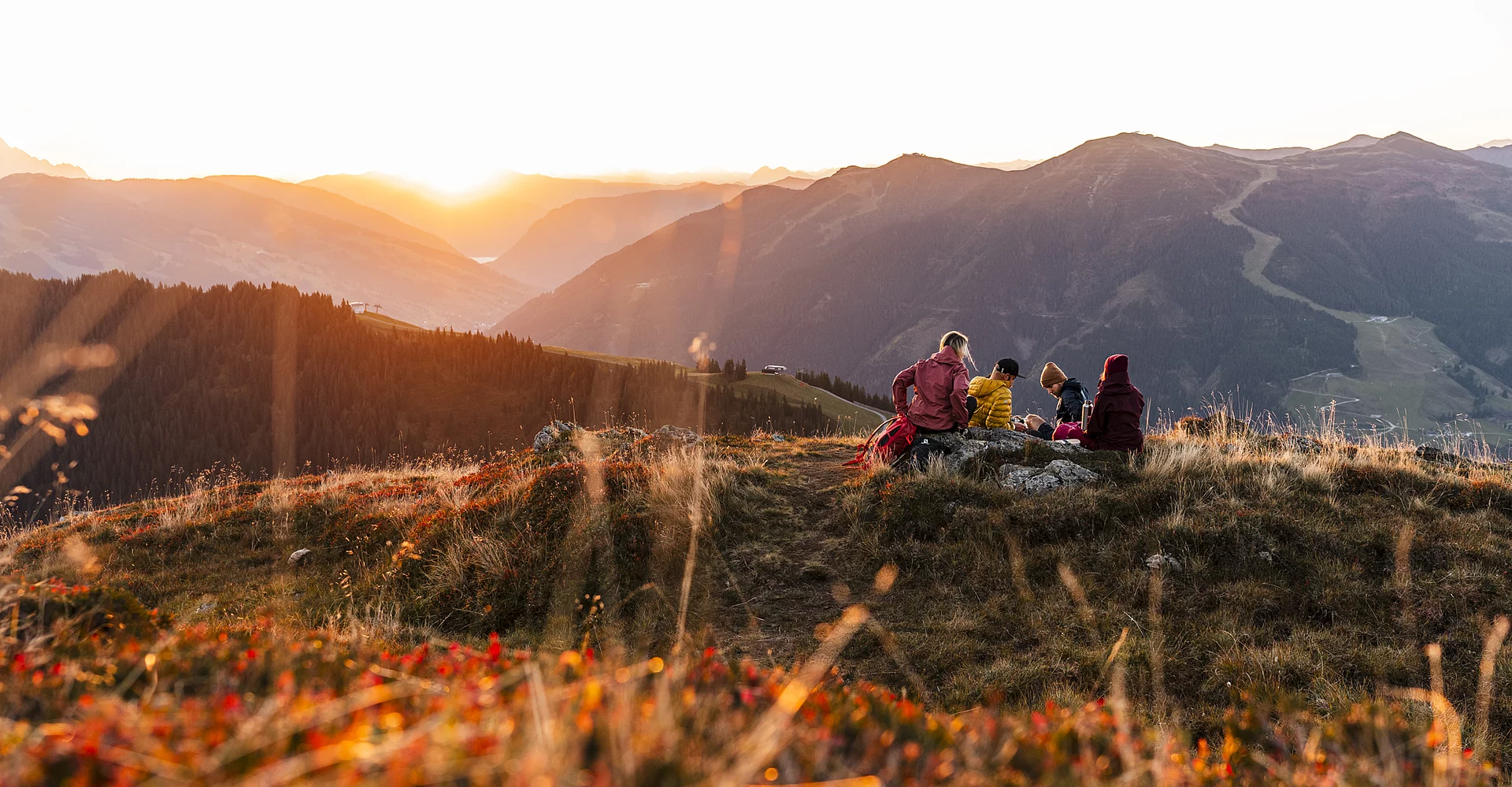 Vier Personen betrachten den Sonnenaufgang im Herbst am Berg in Saalbach Hinterglemm