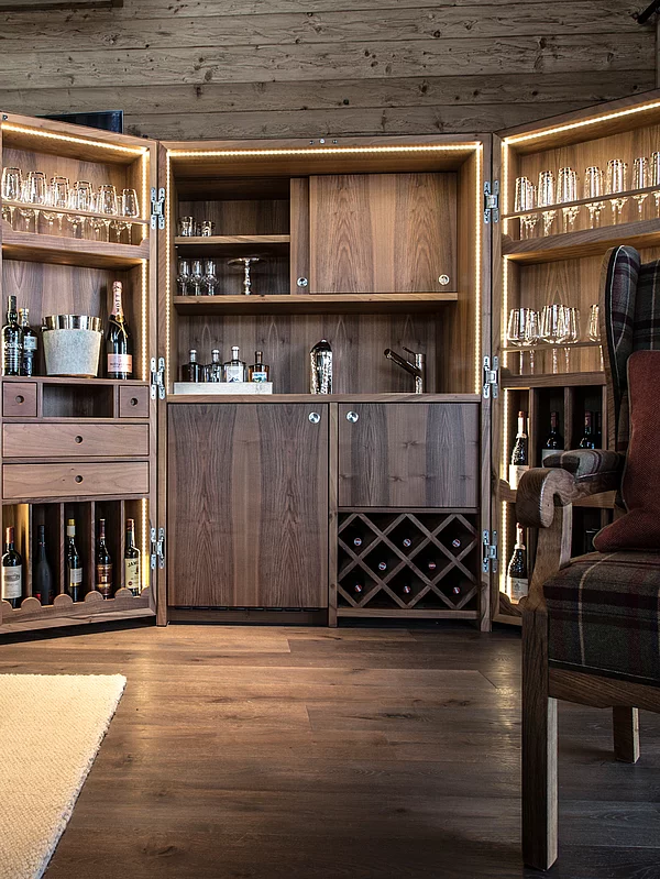 Open house bar with fine wooden furniture, glasses and spirits in the Schmiedalm - the chalet in Saalbach Hinterglemm