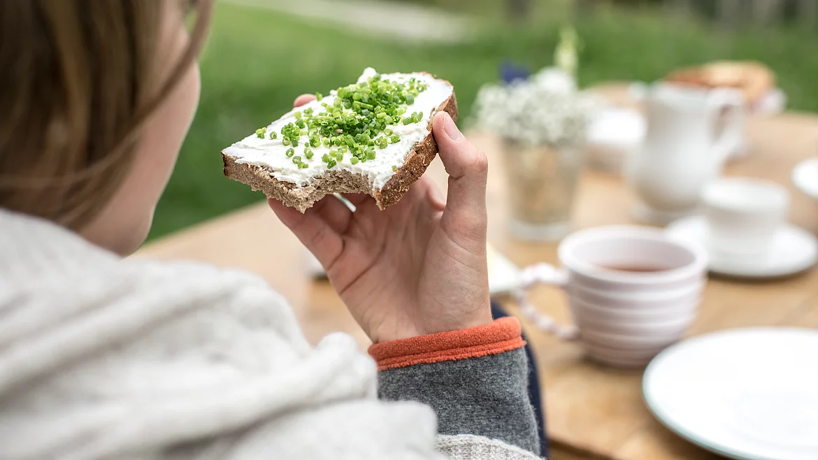 Ein Kind genießt ein frisches Schnittlauchbrot beim Frühstück auf der Schmiedalm.