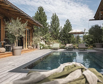 Outdoor-Pool des Chalet Die Schmiedalm in Saalbach Hinterglemm im Sommer mit Chalet und Bergpanorama.