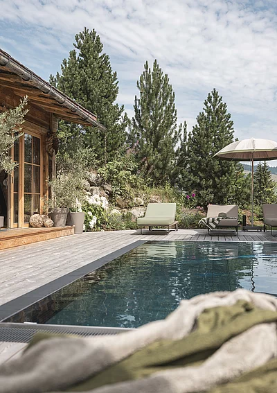 Outdoor-Pool des Chalet Die Schmiedalm in Saalbach Hinterglemm im Sommer mit Chalet und Bergpanorama.