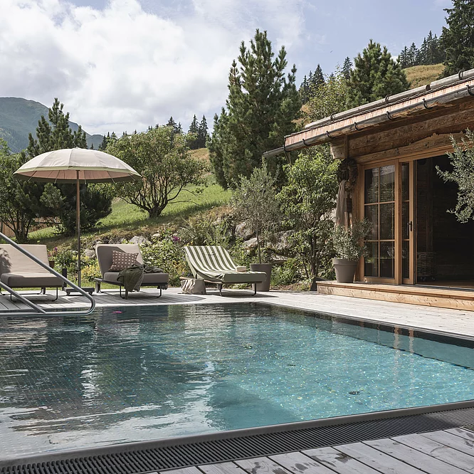 privater Outdoor Pool & Sauna Outdoor-Pool des Chalet Die Schmiedalm in Saalbach Hinterglemm im Sommer mit Chalet und Bergpanorama.