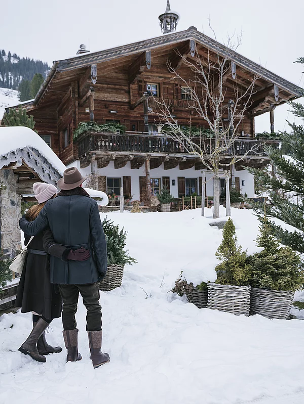 Paar mit Blick auf ein Luxuschalet in den Bergen im Winter