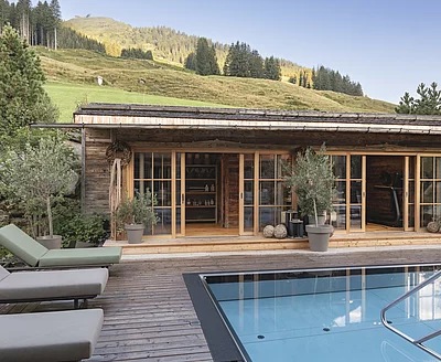 Outdoor-Pool des Chalet Die Schmiedalm in Saalbach Hinterglemm im Sommer mit Chalet und Bergpanorama.