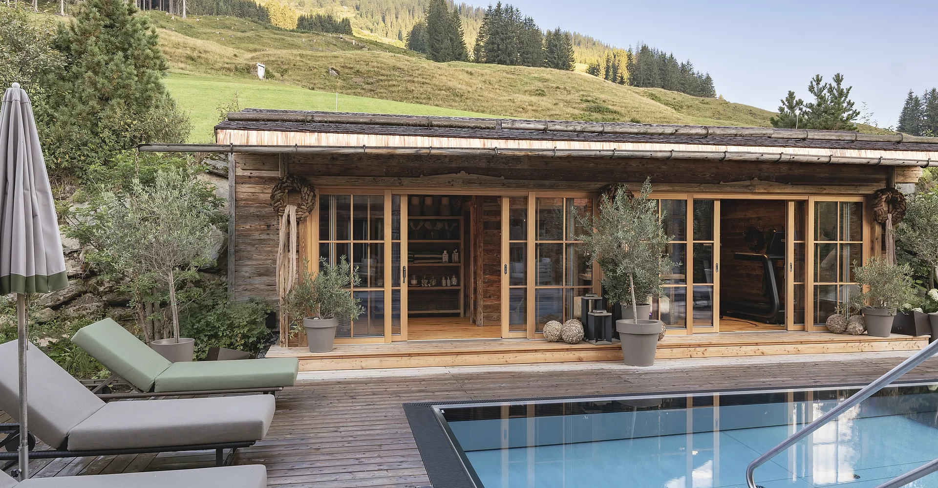 Outdoor-Pool des Chalet Die Schmiedalm in Saalbach Hinterglemm im Sommer mit Chalet und Bergpanorama. 