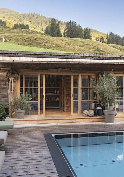 Outdoor-Pool des Chalet Die Schmiedalm in Saalbach Hinterglemm im Sommer mit Chalet und Bergpanorama.