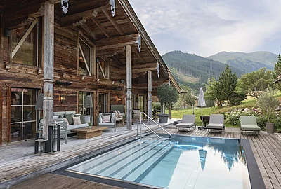 Outdoor-Pool des Chalet Die Schmiedalm in Saalbach Hinterglemm im Sommer mit Chalet und Bergpanorama.